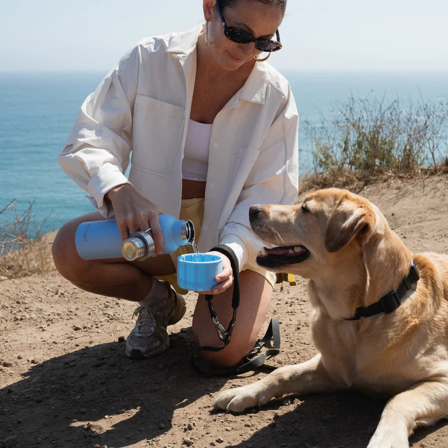 Woman with a dog by the ocean holding a blue water bottle