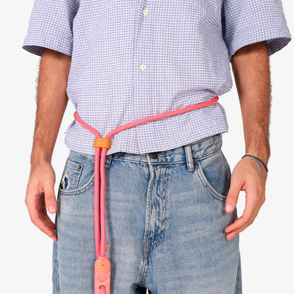 Person wearing a pink leash with an orange buckle, standing against a plain background